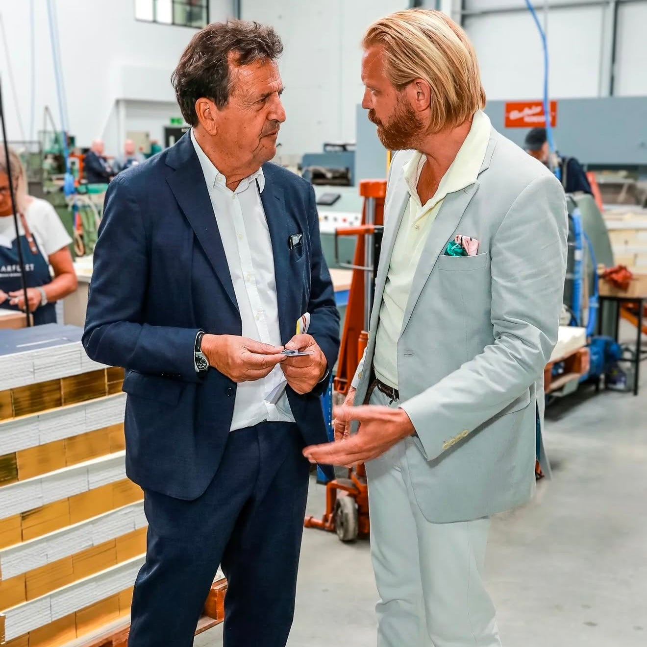 Two men in suits standing in a warehouse setting.